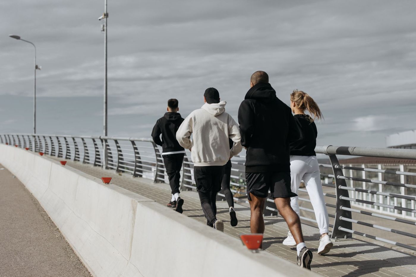 A group of adults jogging across a city bridge