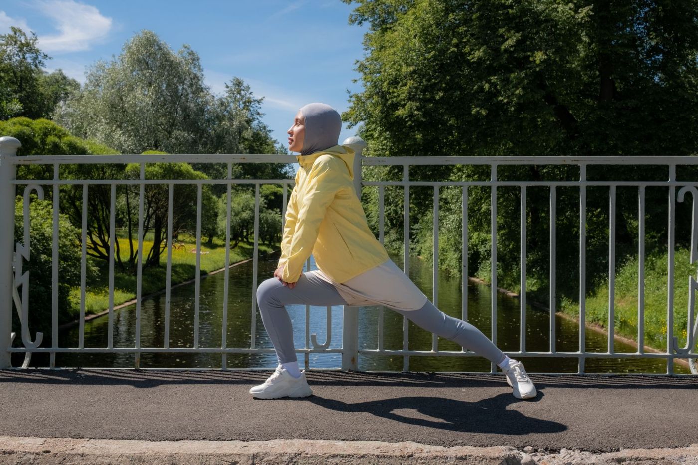 A woman in a hijab stretching on a bridge by a river
